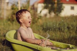 Cute little boy bathing in tub outdoors in garden. Happy child is splashing, playing with water and having fun. Summer season and recreation. Staying cool in the summer heat. Water fun in backyard. photo