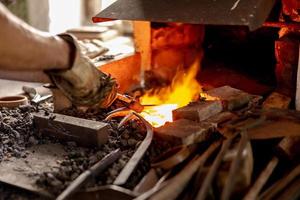 The blacksmith in production process of metal products, handmade in the forge. Craftsman heats metal in the fire. Metal industry, old profession. photo