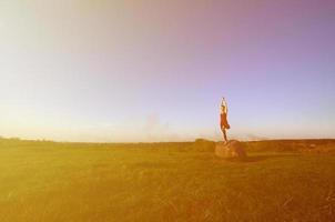 Silhouette of young blonde girl in sport suit practice yoga on a picturesque green hill in the evening at sunset. The concept of exercising and healthy lifestyles photo