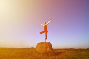 Silhouette of young blonde girl in sport suit practice yoga on a picturesque green hill in the evening at sunset. The concept of exercising and healthy lifestyles photo