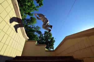 A young guy performs a jump through the space between the concrete parapets. The athlete practices parkour, training in street conditions. Bottom view photo