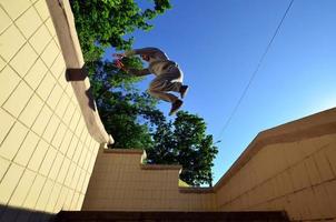 un chico joven realiza un salto a través del espacio entre los parapetos de hormigón. el atleta practica parkour, entrenando en condiciones de calle. vista inferior foto