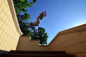 A young guy performs a jump through the space between the concrete parapets. The athlete practices parkour, training in street conditions. Bottom view photo