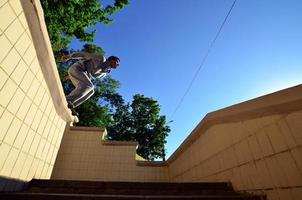 A young guy performs a jump through the space between the concrete parapets. The athlete practices parkour, training in street conditions. Bottom view photo