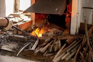 The blacksmith in production process of metal products, handmade in the forge. Craftsman heats metal in the fire. Metal industry, old profession. photo