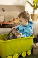 Little caucasian boy with blue hoodie playing with colourful toys at home. Child having fun. Happy and cheerful kid plays with ship, dinosaurs, castle. Leisure activity, domestic life. Cozy room. photo