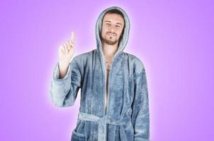 Portrait of young caucasian bearded man in blue bathrobe shows attention gesture isolated on violet background photo