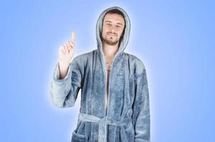 Portrait of young caucasian bearded man in blue bathrobe shows attention gesture isolated on blue background photo