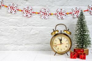 Decorative christmas tree, gift boxes and alarm clock on white wooden background. photo