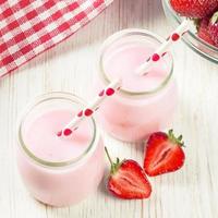 Strawberry milkshake in the glass jar on white wooden background photo