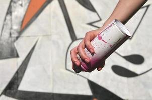 foto de la mano de una niña con latas de pintura en aerosol en las manos sobre un fondo de pared de graffiti. el concepto de arte callejero y uso de pinturas en aerosol. imagen de fondo de la tienda de arte de graffiti