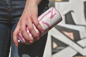 foto de la mano de una niña con latas de pintura en aerosol en las manos sobre un fondo de pared de graffiti. el concepto de arte callejero y uso de pinturas en aerosol. imagen de fondo de la tienda de arte de graffiti