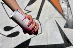 foto de la mano de una niña con latas de pintura en aerosol en las manos sobre un fondo de pared de graffiti. el concepto de arte callejero y uso de pinturas en aerosol. imagen de fondo de la tienda de arte de graffiti