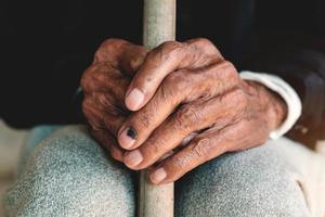 Asian old man sitting with his hands on a walking stick. photo