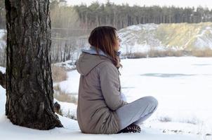 A young Caucasian girl in a brown coat staring into the distance on the horizon line between the sky and the frozen lake in winter photo