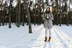 una joven y alegre chica caucásica con un abrigo marrón sostiene una bola de nieve en un bosque cubierto de nieve en invierno. foto de ojo de pez