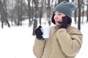 retrato invernal de una joven con smartphone y taza de café foto