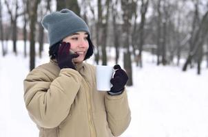 retrato invernal de una joven con smartphone y taza de café foto