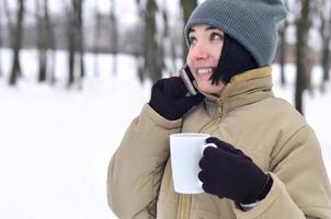 retrato invernal de una joven con smartphone y taza de café foto