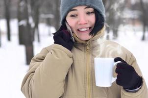 Winter portrait of young girl with smartphone and coffee cup photo