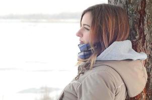 una joven caucásica con un abrigo marrón mirando a lo lejos en la línea del horizonte entre el cielo y el lago congelado en invierno foto