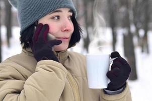 retrato invernal de una joven con smartphone y taza de café foto