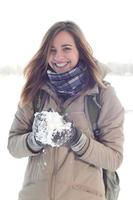 A young and joyful Caucasian girl in a brown coat holds a snowball in the background of a horizon line between the sky and a frozen lake in winter photo