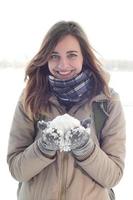 A young and joyful Caucasian girl in a brown coat holds a snowball in the background of a horizon line between the sky and a frozen lake in winter photo