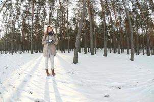 A young and joyful Caucasian girl in a brown coat holds a snowball in a snow-covered forest in winter. Fisheye Photo