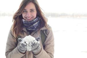 A young and joyful Caucasian girl in a brown coat holds a snowball in the background of a horizon line between the sky and a frozen lake in winter photo