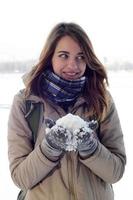 A young and joyful Caucasian girl in a brown coat holds a snowball in the background of a horizon line between the sky and a frozen lake in winter photo