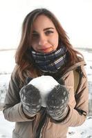 una joven y alegre chica caucásica con un abrigo marrón sostiene una bola de nieve frente a una línea de horizonte entre el cielo y un lago congelado en invierno. foto de ojo de pez