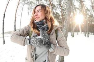 A young and joyful Caucasian girl in a brown coat sculpts a snowball in a snow-covered forest in winter. Games with snow in the open air. Fisheye Photo