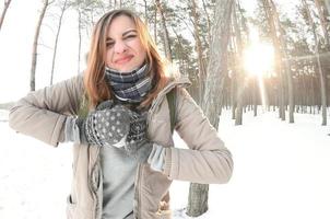 A young and joyful Caucasian girl in a brown coat sculpts a snowball in a snow-covered forest in winter. Games with snow in the open air. Fisheye Photo