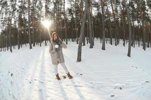 A young and joyful Caucasian girl in a brown coat holds a snowball in a snow-covered forest in winter. Fisheye Photo