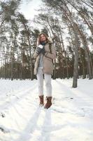 una joven y alegre chica caucásica con un abrigo marrón sostiene una bola de nieve en un bosque cubierto de nieve en invierno. foto de ojo de pez