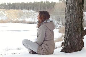 A young Caucasian girl in a brown coat staring into the distance on the horizon line between the sky and the frozen lake in winter photo