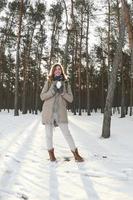 una joven y alegre chica caucásica con un abrigo marrón sostiene una bola de nieve en un bosque cubierto de nieve en invierno. foto de ojo de pez