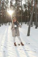 una joven y alegre chica caucásica con un abrigo marrón sostiene una bola de nieve en un bosque cubierto de nieve en invierno. foto de ojo de pez