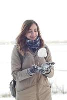 A young and joyful Caucasian girl in a brown coat holds a snowball in the background of a horizon line between the sky and a frozen lake in winter photo