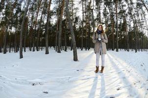 A young and joyful Caucasian girl in a brown coat holds a snowball in a snow-covered forest in winter. Fisheye Photo