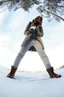 A young and joyful Caucasian girl in a brown coat holds a snowball in front of a horizon line between the sky and a frozen lake in winter. Fisheye Photo