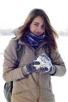 A young and joyful Caucasian girl in a brown coat holds a snowball in the background of a horizon line between the sky and a frozen lake in winter photo