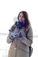 A young and joyful Caucasian girl in a brown coat holds a snowball in the background of a horizon line between the sky and a frozen lake in winter photo