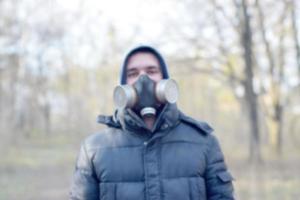 Blurred portrait of young man in protective gas mask outdoors in spring wood photo