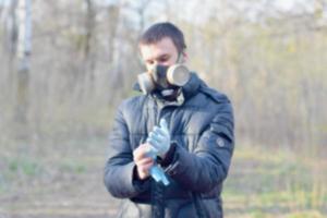 Blurred portrait of young man in protective gas mask wears rubber disposable gloves outdoors in spring wood photo