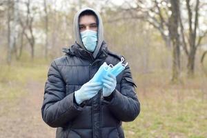 Young man in protective mask shows bunch of protective face masks outdoors in spring wood photo