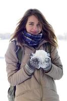 A young and joyful Caucasian girl in a brown coat holds a snowball in the background of a horizon line between the sky and a frozen lake in winter photo