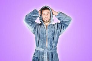 Portrait of young caucasian bearded man in blue bathrobe shows confused face emotion isolated on violet background photo