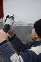 un trabajador anciano perfora un agujero en una pared de espuma de poliestireno para la posterior instalación de una espiga de refuerzo de plástico. creando agujeros en la pared con un taladro. calentamiento de la fachada del edificio foto